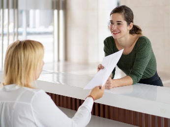 A woman handing an envelope to a person behind a desk.